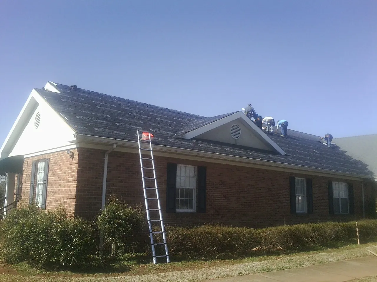 Crew tearing shingles off a brick ranch roof with a ladder set — Metal Roof Repair work by our crew in Saco