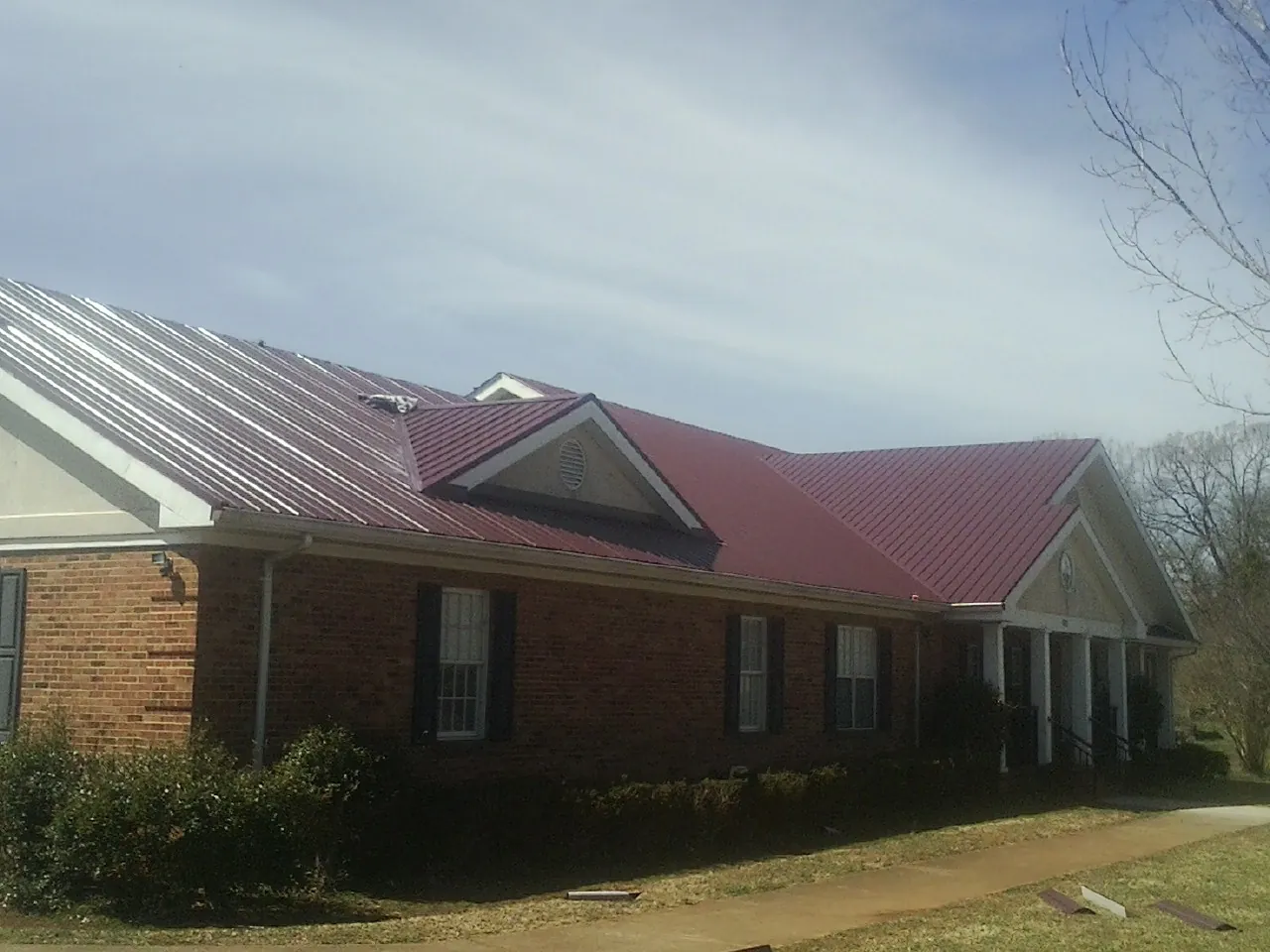 Red metal roof with gabled entries on a long brick building, from a Hail Damage Roof Repair job in Saco