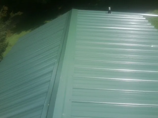New green metal panels meeting at the ridge of a roof — Flat Roof Repair work by our crew in Saco