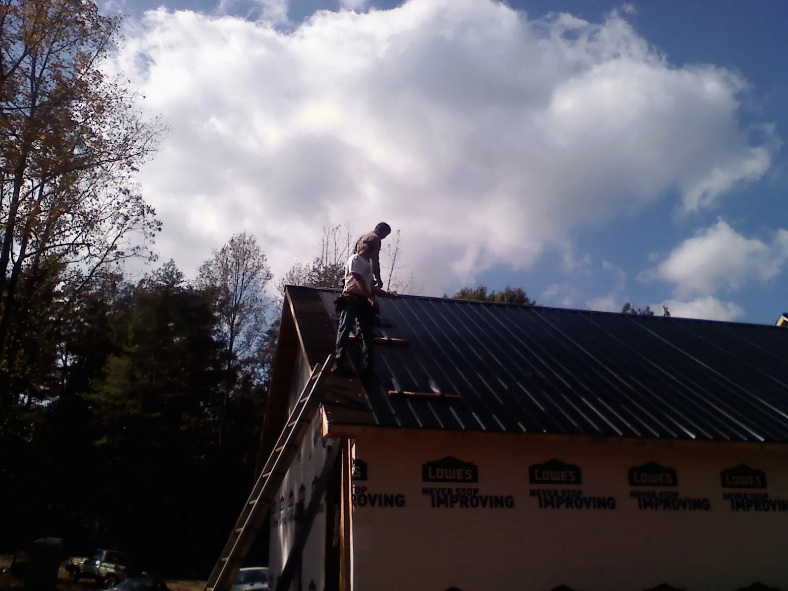 Roofer fastening dark metal panels high against a cloudy sky, from a Roof Inspection job in Saco