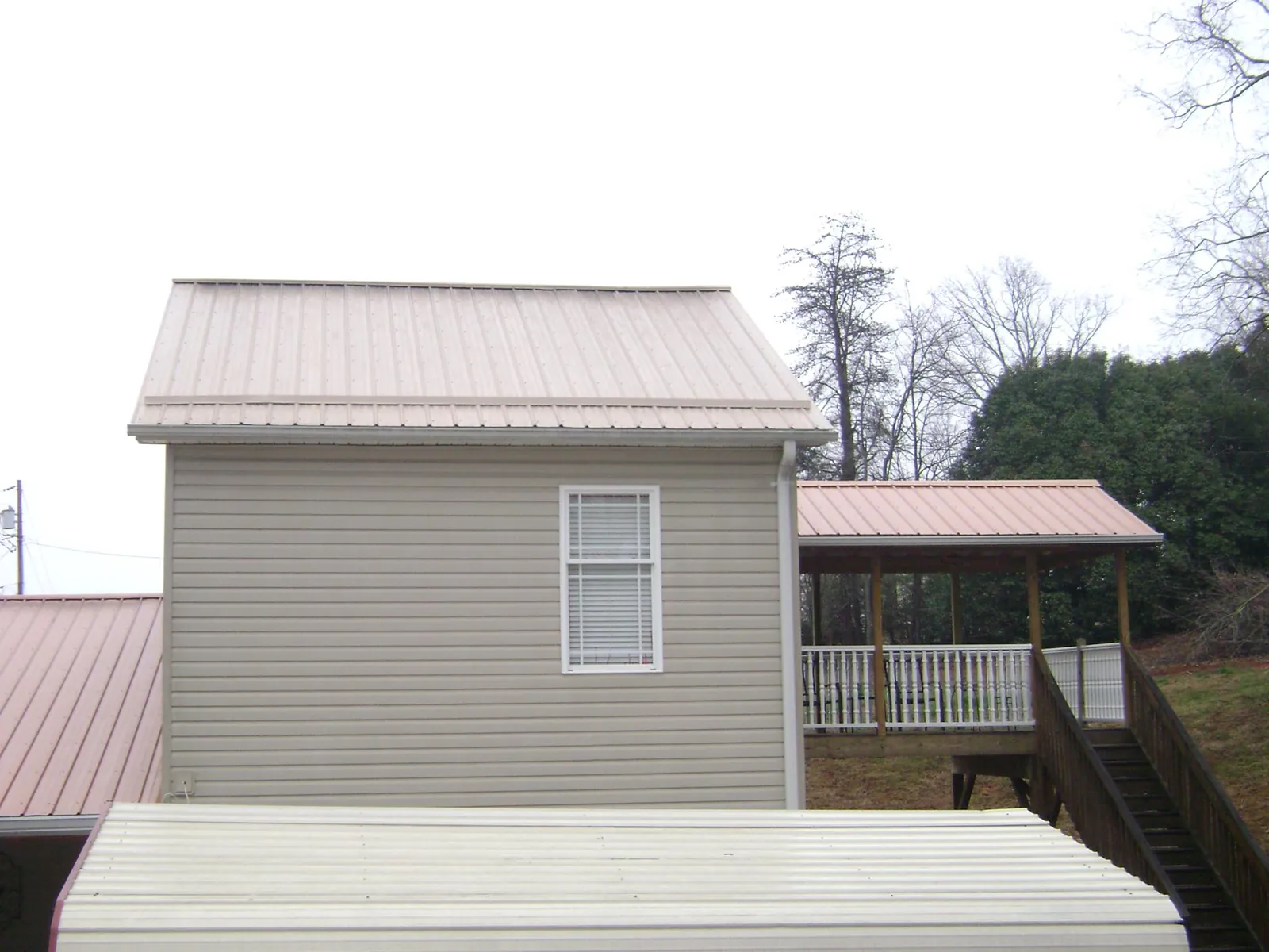 Tan metal roofs on a two story addition and attached porch, from a Roof Replacement job in Saco